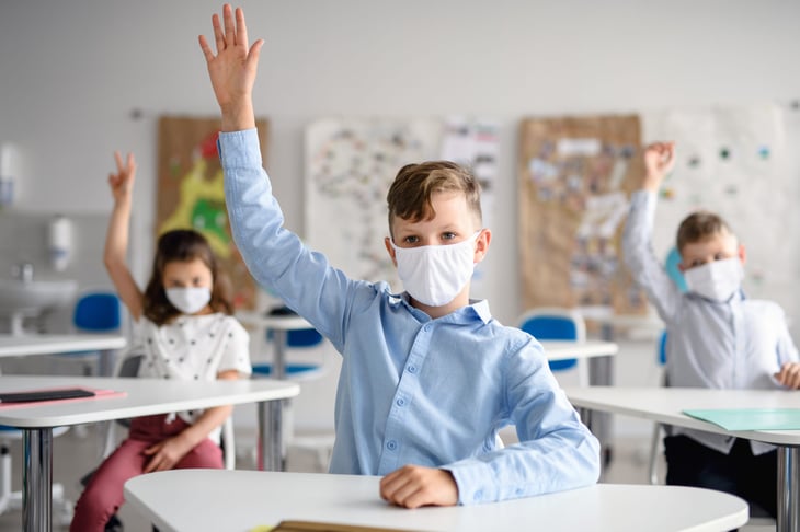 Student in face mask raising hand