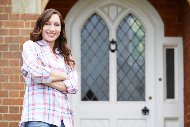 A woman stands outside the front door of her home