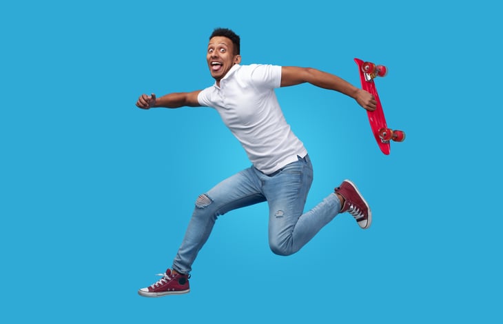 excited young African American man red skateboard jumping blue background
