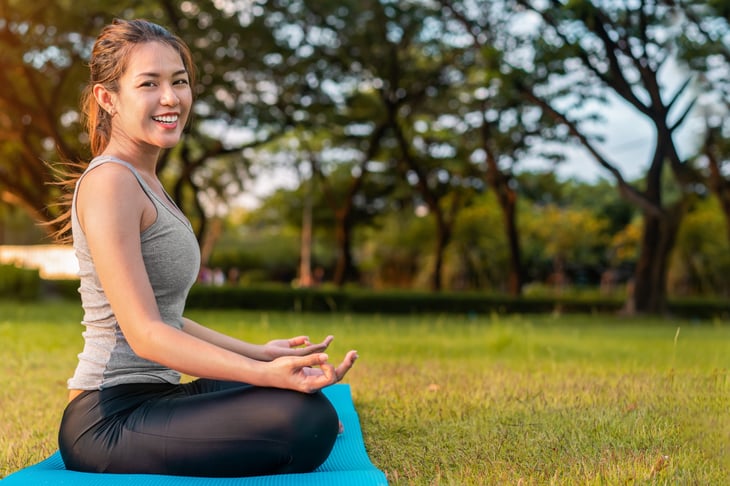 Happy young Asian woman meditating outdoors
