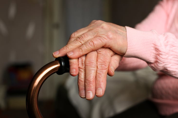 An elderly woman rests her hands on her walking cane