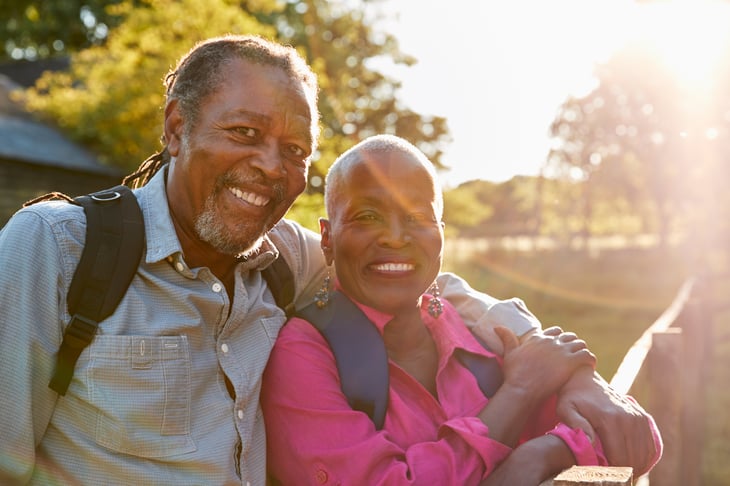 An older black couple hikes with backpacks as the sun sets