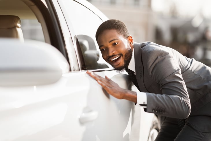 A young man in a business suit looks at a car