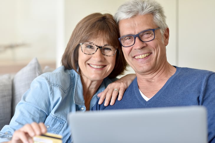 An older couple in glasses uses a laptop computer to shop online