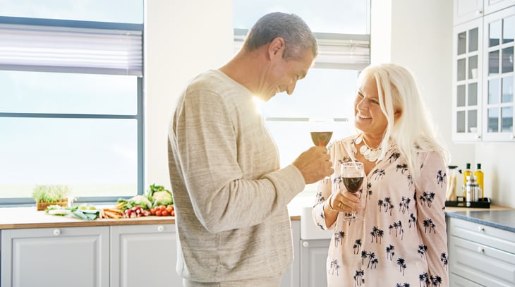 Happy retired couple red wine toast white kitchen