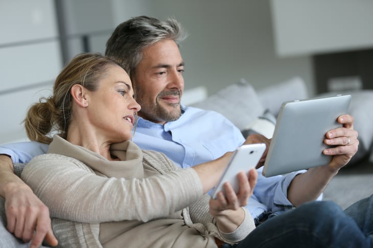 A couple uses a tablet computer and smartphone on the couch