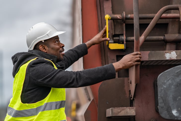 railroad engineer wearing safety equipment (helmet and jacket) checking gear train