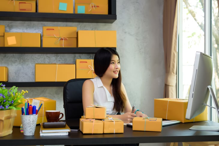 Woman sits at a desk surrounded by shipping boxes