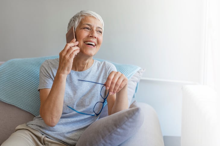 Senior woman talking on her mobile phone. Senior woman has a happy conversation at cellphone. Smiling senior woman using phone sitting on couch at home. - Image