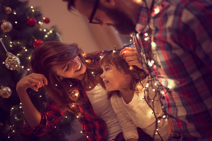 Family decorating a Christmas tree with lights