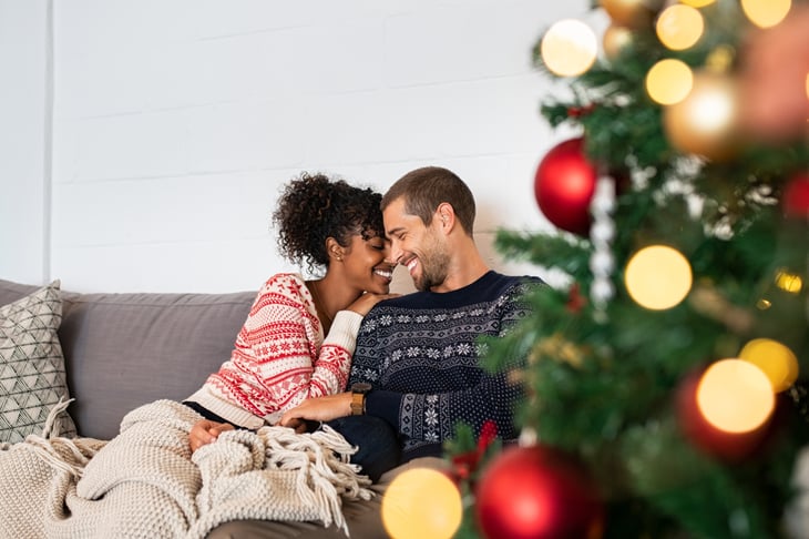 A young couple snuggles in front of a Christmas tree