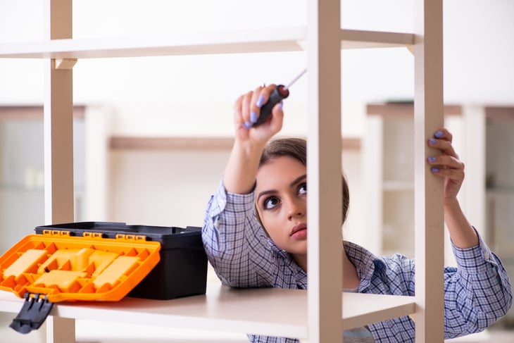 A young woman with a toolbox assembles a bookshelf