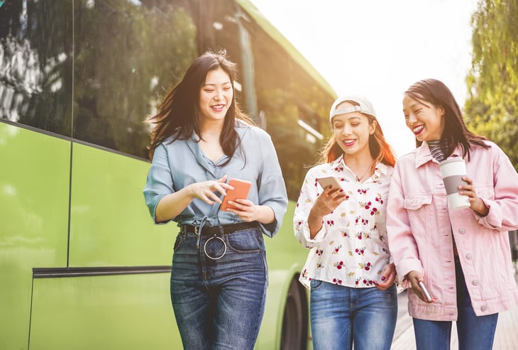 friends using smartphones at a bus station