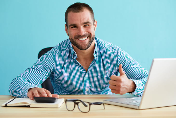 Happy young man smiling and giving a thumbs up while doing his taxes on a laptop
