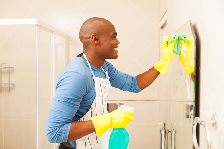 cheerful man cleaning bathroom mirror at home
