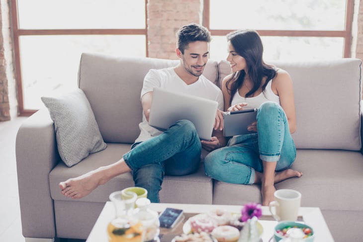 A couple shops online using a laptop computer from their living room sofa