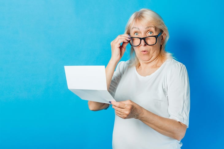 An older woman lowers her eyeglasses in surprise while holding a document