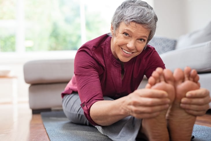 A senior stretches her legs while on a yoga mat during a workout at home