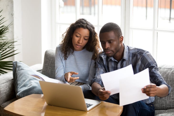 A young couple review financial documents over a laptop computer in their living room