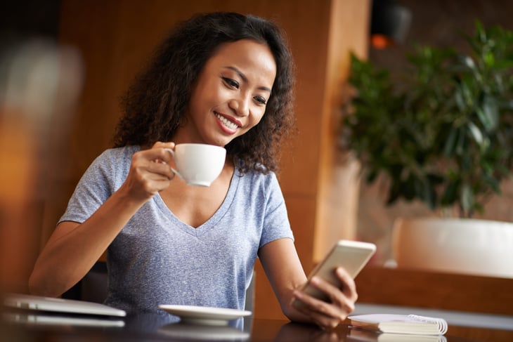 A woman uses an investing app for beginners while drinking her coffee