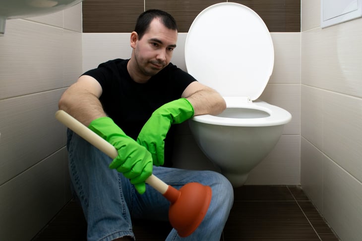 Man with plunger next to toilet
