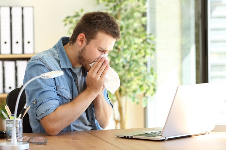 A man blowing his nose at his desk