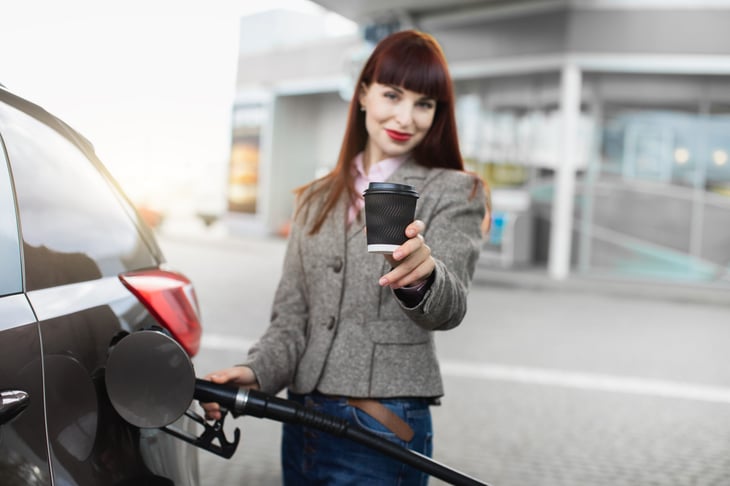 Woman holding coffee while pumping gas