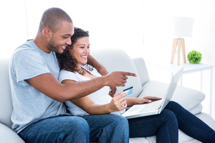 Couple on the couch with laptop and credit card spending their credit card rewards points