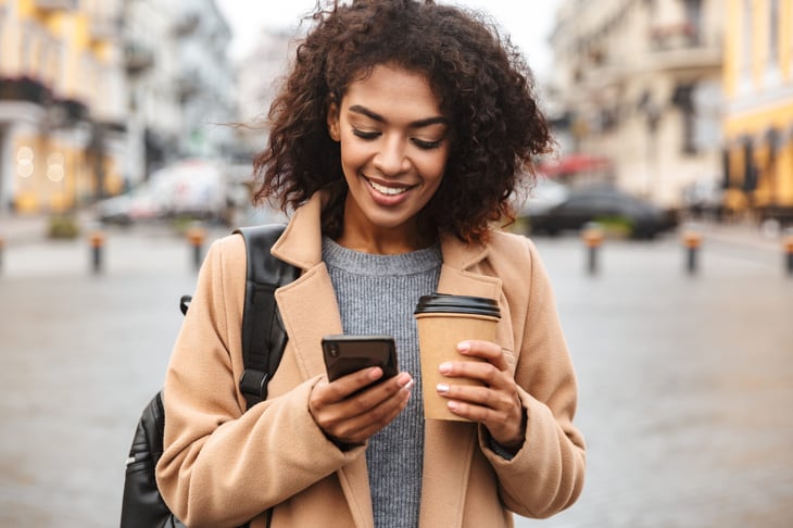 Happy woman walking with phone and coffee