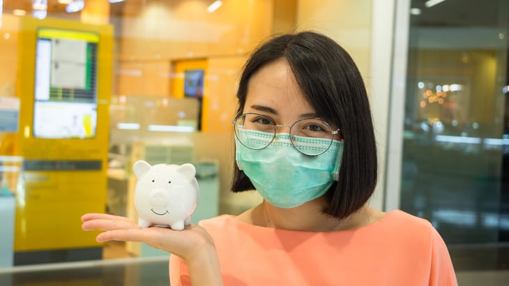 A woman in a mask holds a piggy bank at a bank