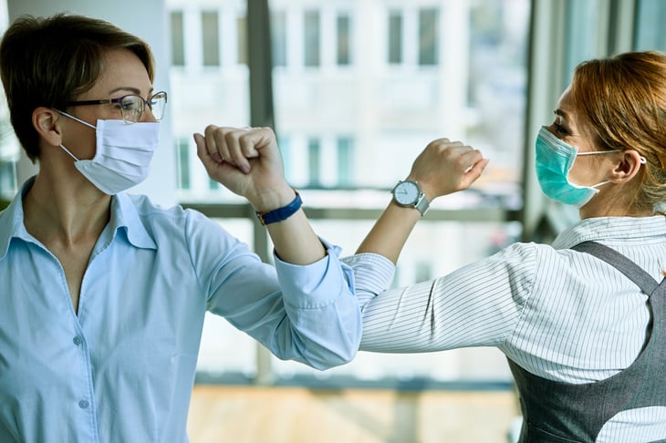 businesswoman in masks bump elbows at work