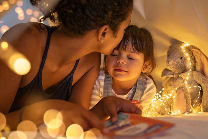Woman mother mom kissing child in tent fairy lights