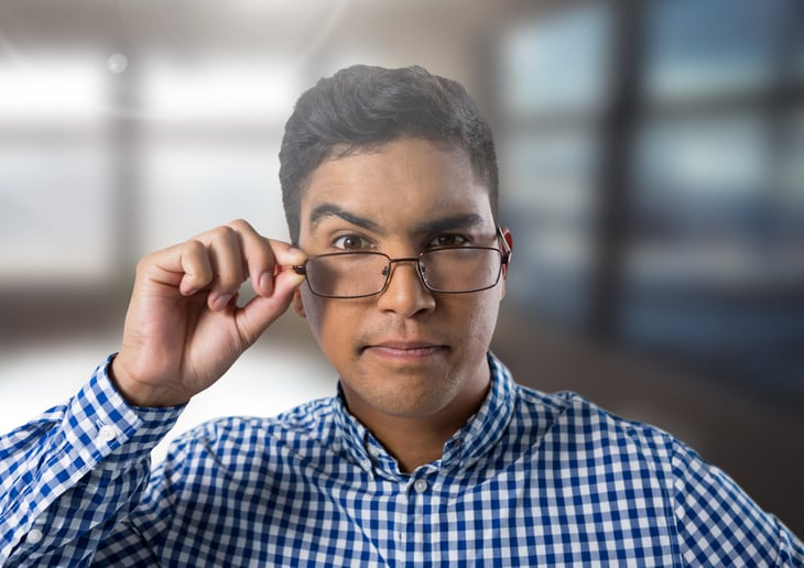 A skeptical worker raises an eyebrow while lowering his glasses