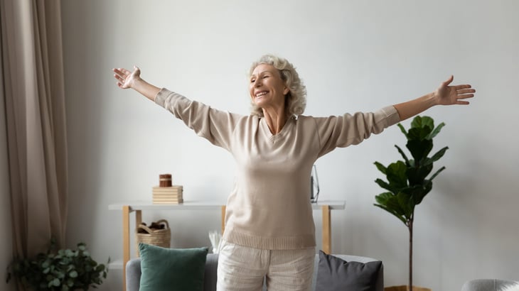 Happy senior stretching out her arms at home