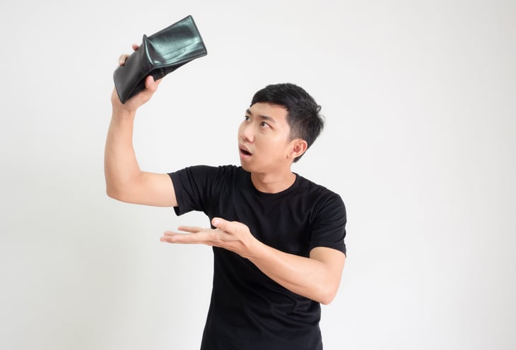 A surprised man looks at his empty wallet in shock