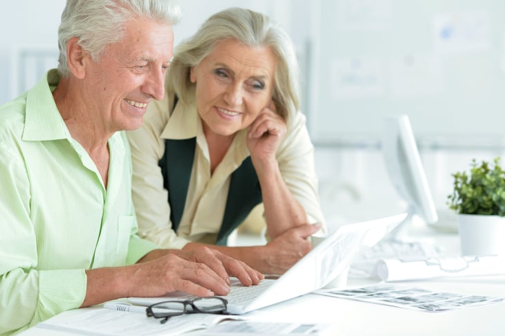 Seniors happily comparing retirement plans on a laptop