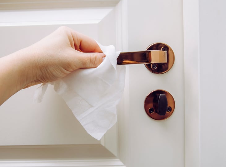 Woman using a disinfecting wipe to clean a door handle