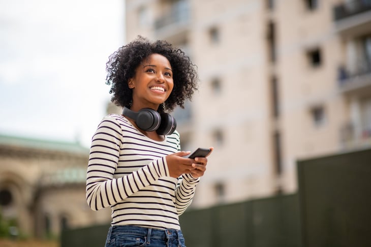 A woman with headphones uses her phone while walking outdoors