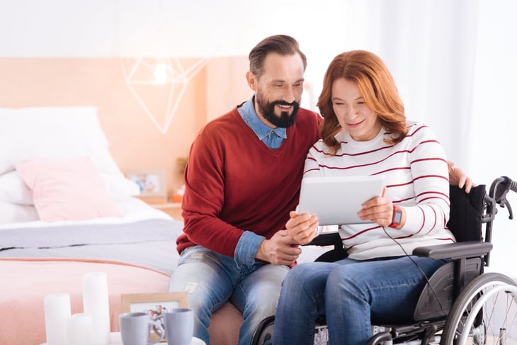 man and woman in a wheelchair smile while using a tablet