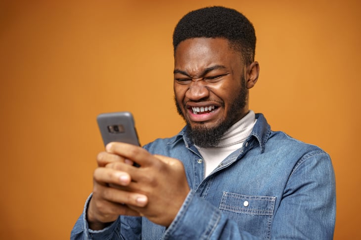 Upset man wincing while looking at his phone