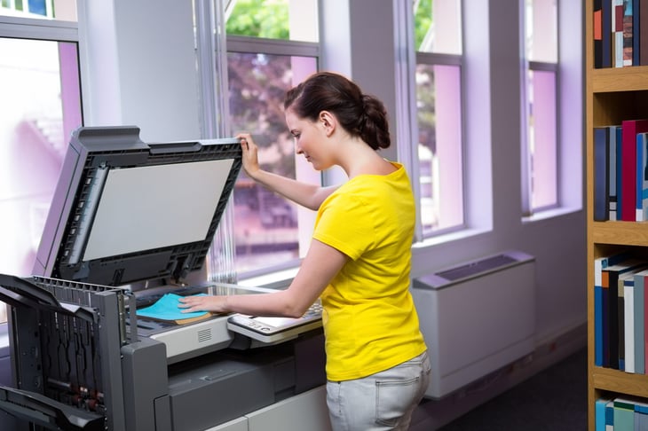 Female student using a photocopier to copy a textbook