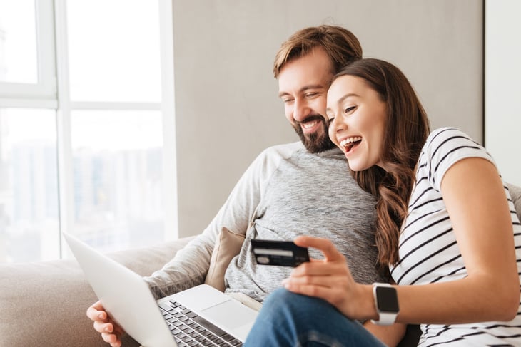 Happy couple using new credit card to shop online on laptop