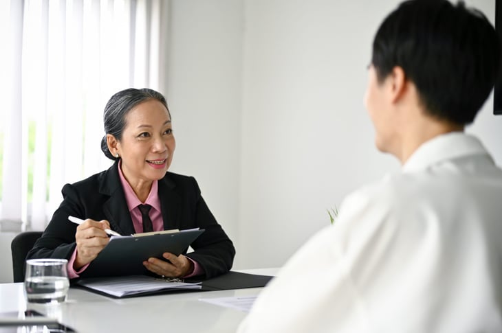 Senior businesswoman or older worker smiling and using a clipboard or tablet to take notes during an interview or meeting