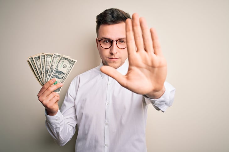 Man giving the stop gesture with one hand and holding cash with the other