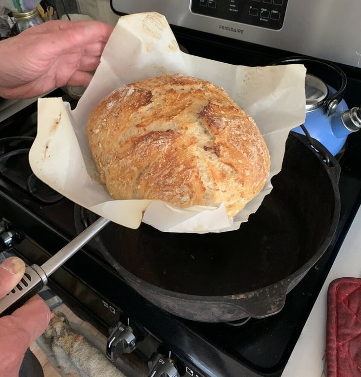 Using a pancake turner to remove rustic bread and parchment paper from a Dutch oven