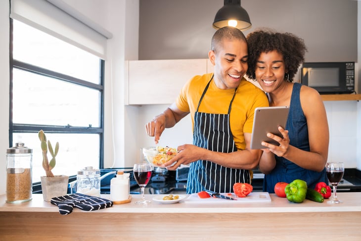 Happy couple using a tablet while cooking