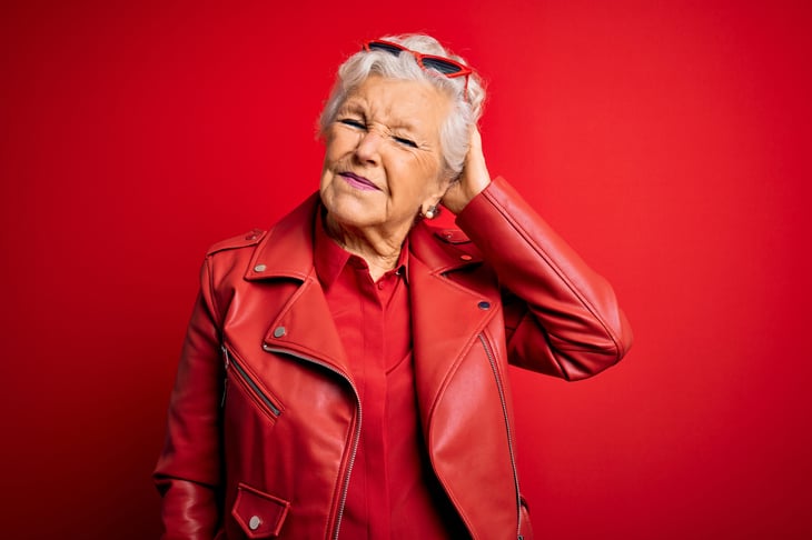 senior older woman red jacket scratches head