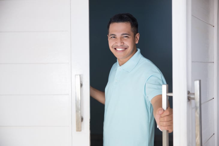 Happy man opening the front door of his home