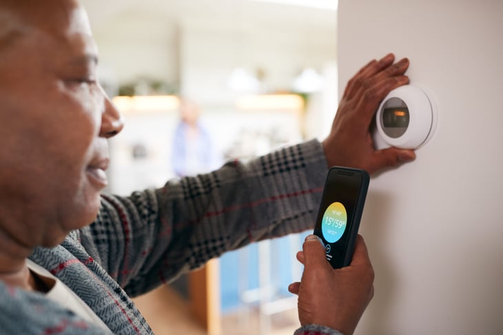 Older Man Using App On Phone To Control Digital Central Heating Thermostat At Home