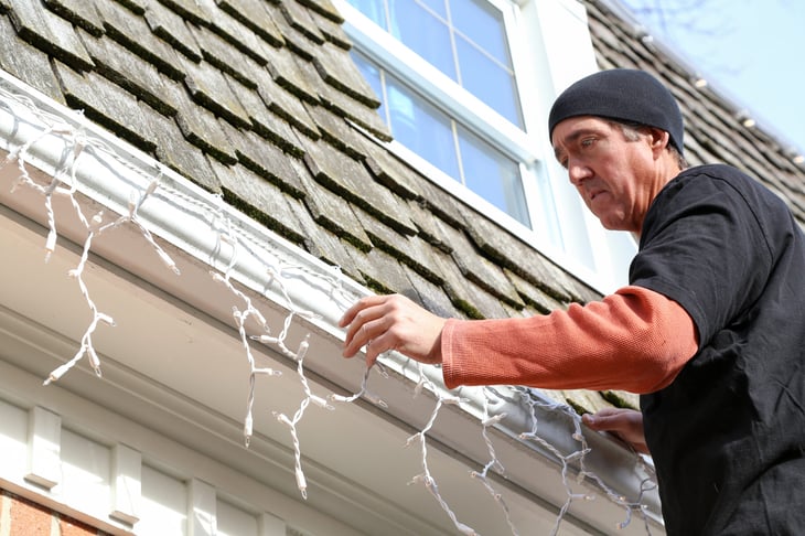 Man hanging holiday lights on the roof of his house